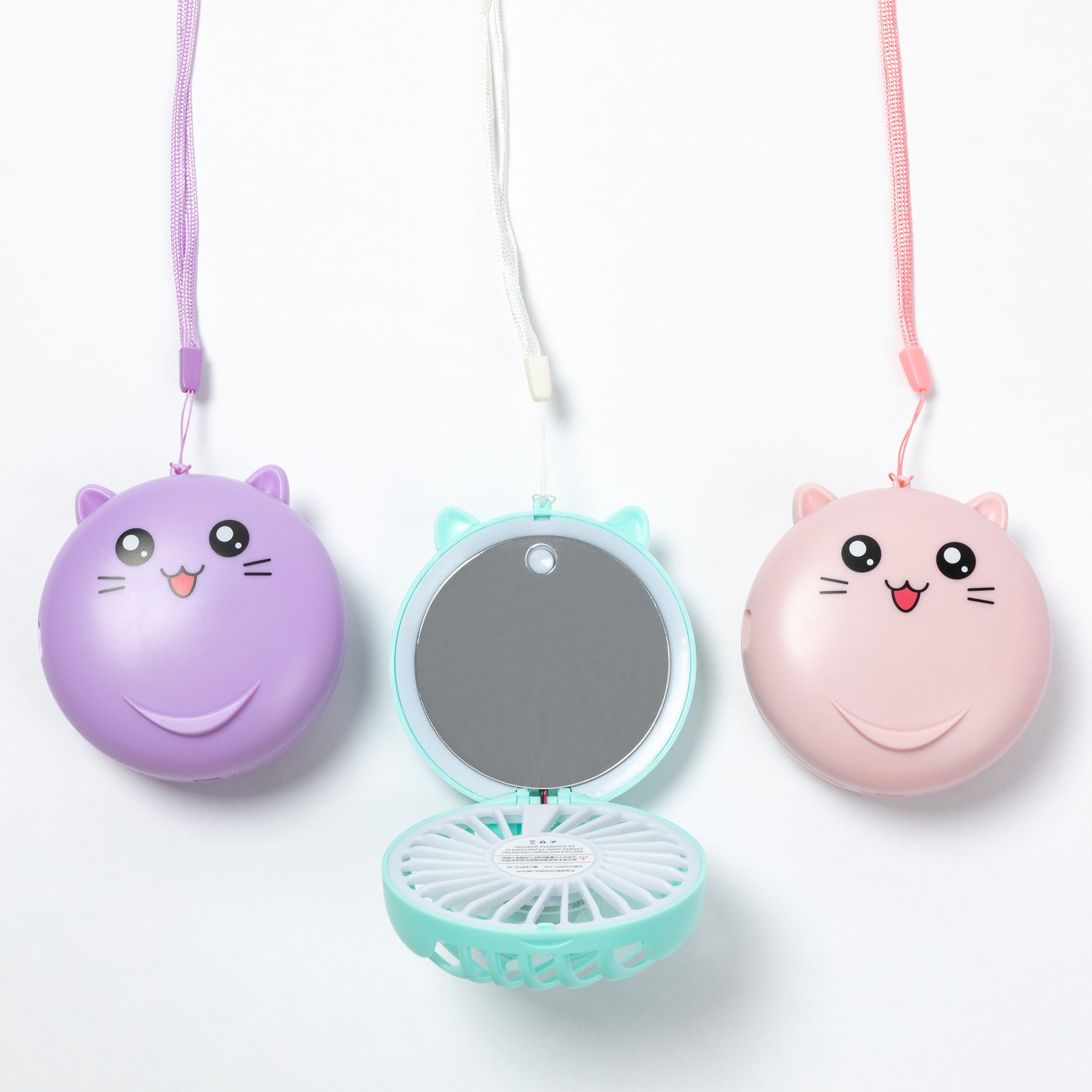 Three cute cat-face compact fans hanging on white strings against a white background. The left fan is purple and closed, the center fan is mint green and open showing a mirror and fan blades, and the right fan is pink and closed.