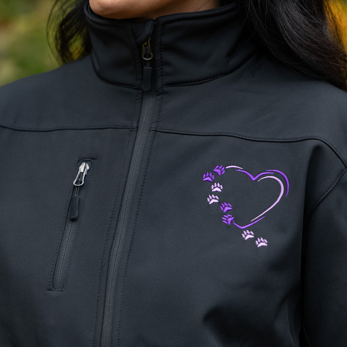 Close-up of a person wearing a black zip-front jacket with a purple heart outline and paw-print graphic on the chest.