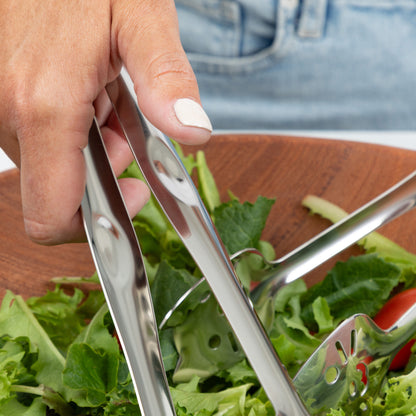 Person using stainless steel tongs to serve fresh salad from a wooden bowl.