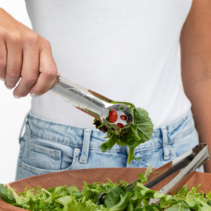 Person using tongs to serve fresh salad from a wooden bowl.