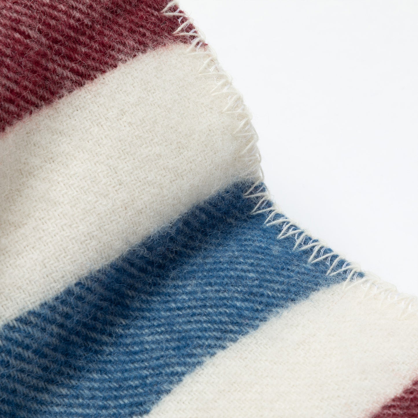 Close-up of a striped knit fabric with white, cream, blue, and burgundy bands, showing the texture and frayed edge.