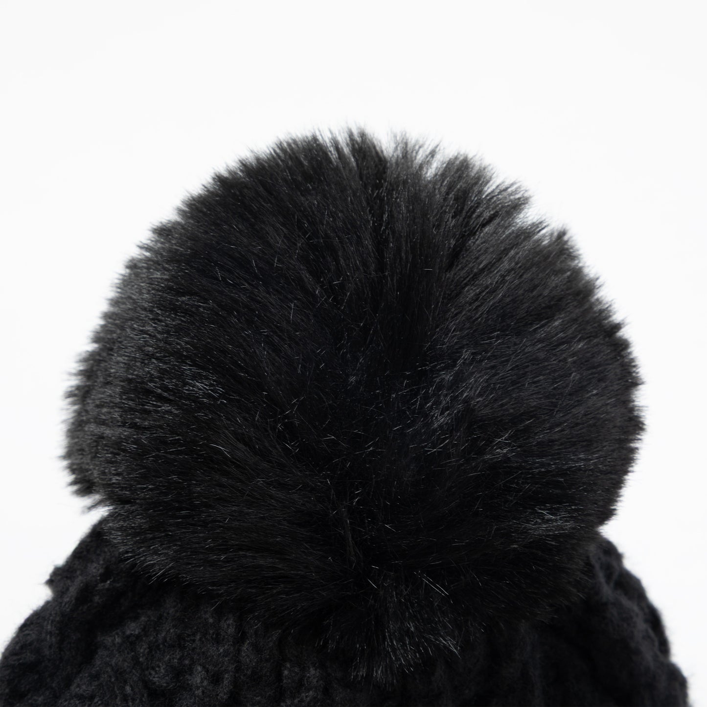 Close-up of a black knit beanie with a large fluffy faux-fur pom-pom on a plain white background.