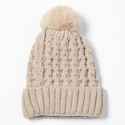 A beige cable-knit beanie hat with a matching faux-fur pom-pom on top, shown against a plain white background.