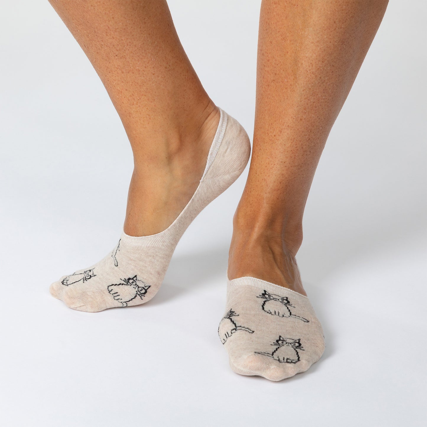 Beige socks with cat prints worn by a person on a light gray background