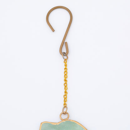 Gold hook hanging a pet shaped wind chime with a white background.