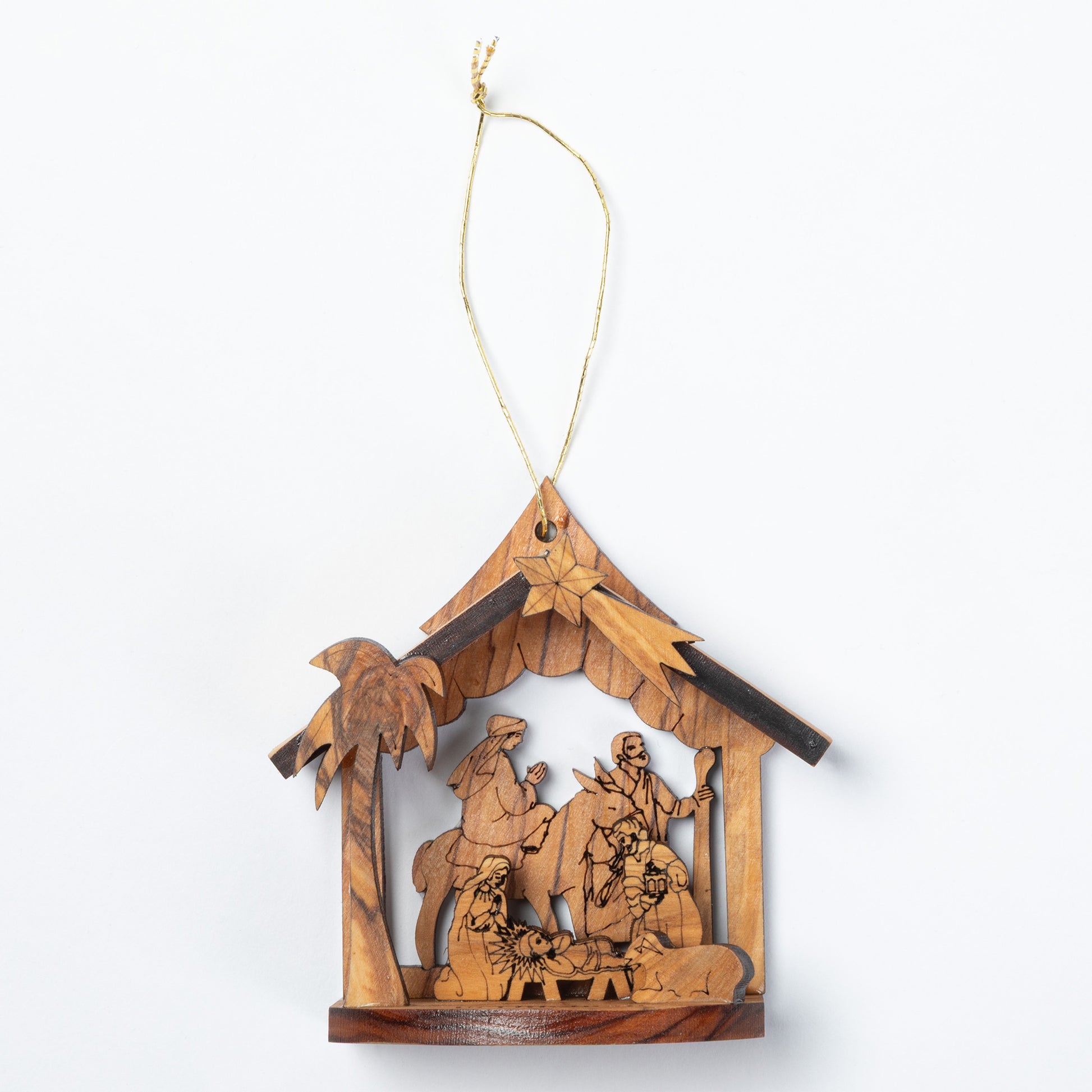 A handcrafted wooden nativity scene ornament hanging from a thin string. The ornament features a house-shaped frame with a star at the peak, carved figures of the Holy Family, animals, and a palm tree, all made from light and dark natural wood tones.
