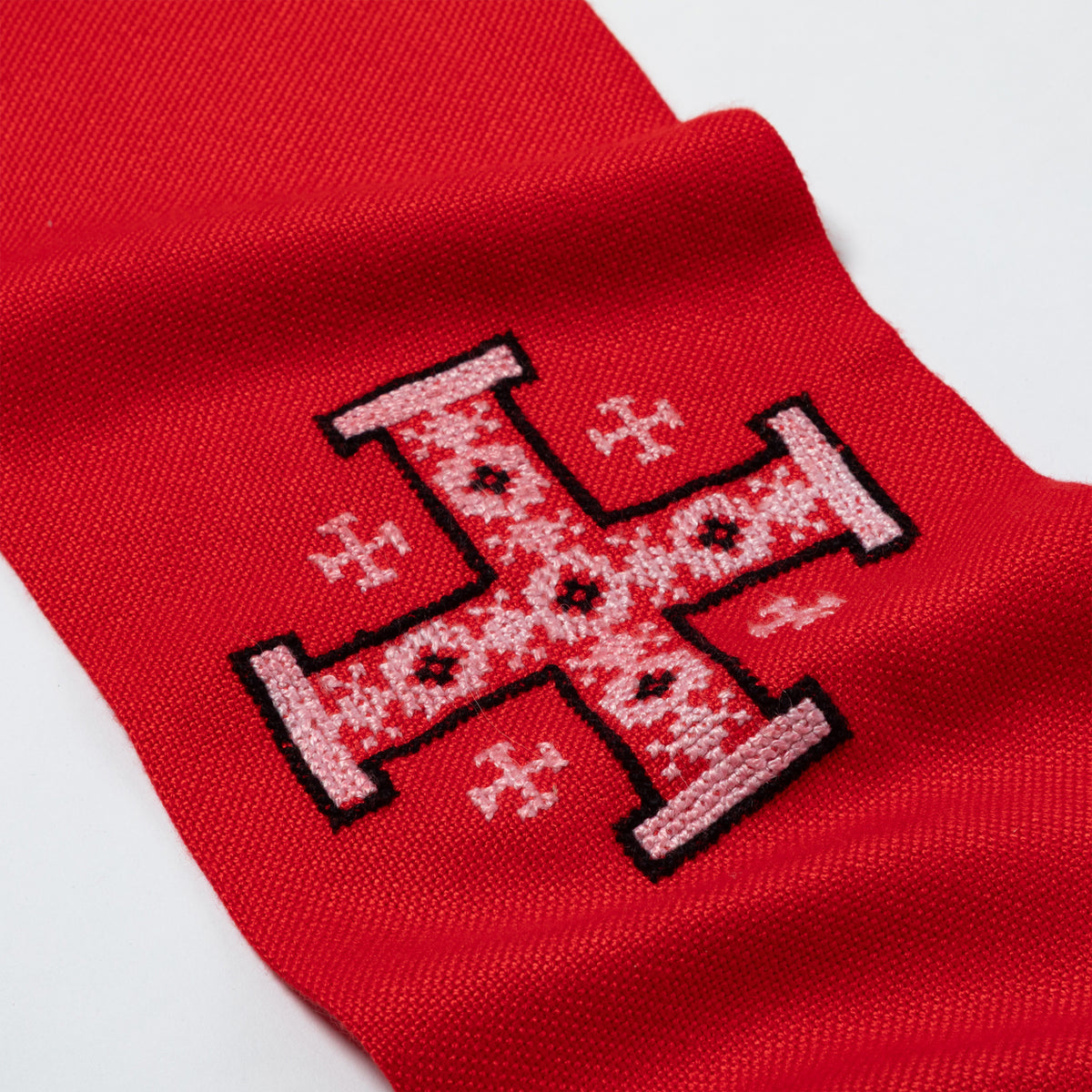 A close-up of a red knit fabric scarf, featuring a large embroidered cross design in white and black.