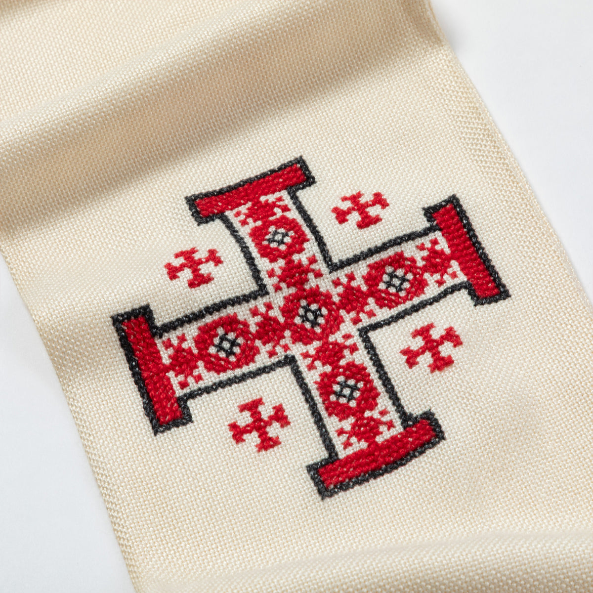 Close-up of a cream-colored woven textile featuring a large red embroidered cross with black outlines and smaller red cross motifs on a white background.