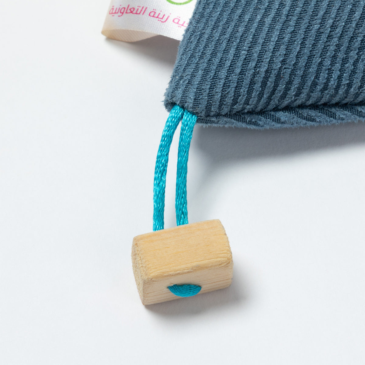 A close-up of a textured slate blue fabric with a bright turquoise blue cord and a small natural wood bead, on a white background.