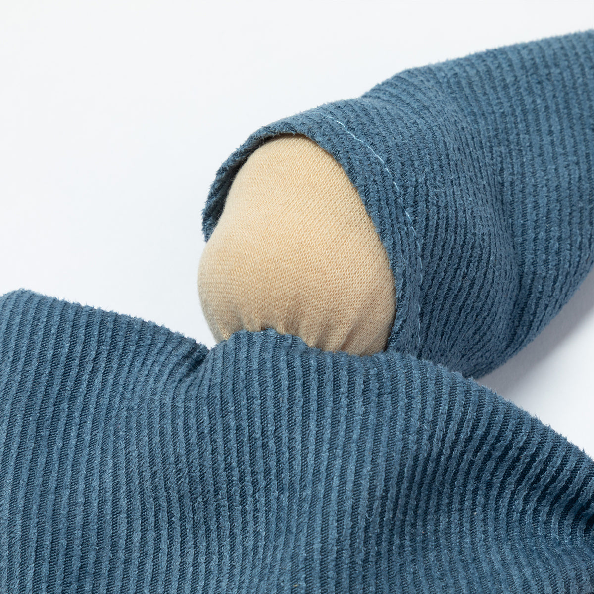 A close-up a blue fabric doll with a wooden pom-pom on the tip of the hat, a wooden pom-pom on the bottom corner, and a small white tag attached.
