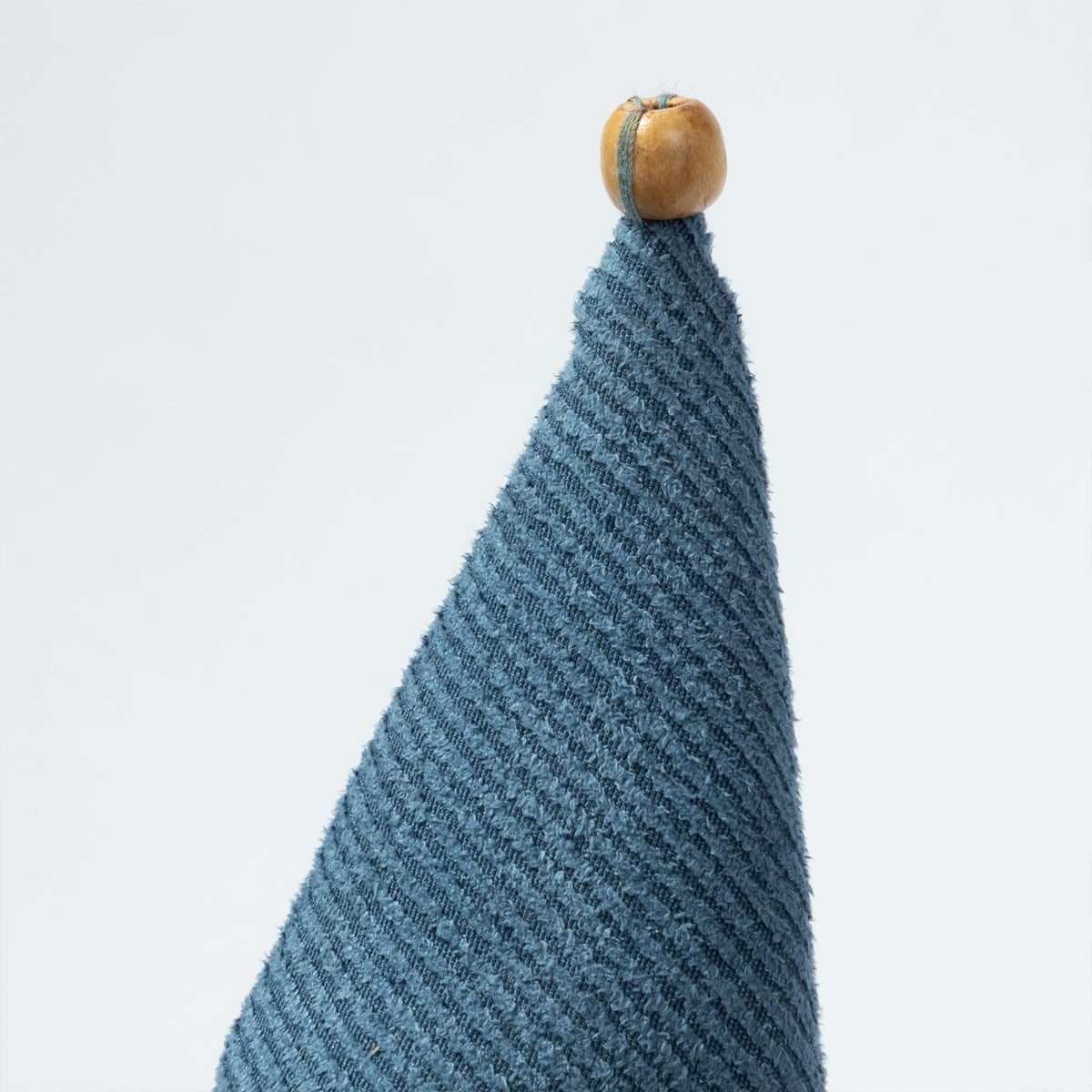 A close-up of a textured blue knit fabric cone with a small round wooden bead finial on top.