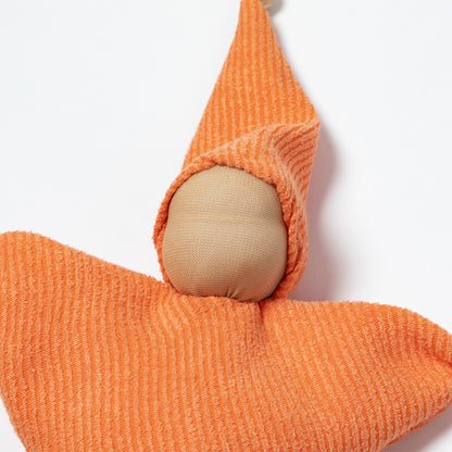 An orange ribbed fabric doll with a wooden pom-pom on the tip of the hat, a wooden pom-pom on the bottom corner, and a small white tag attached.