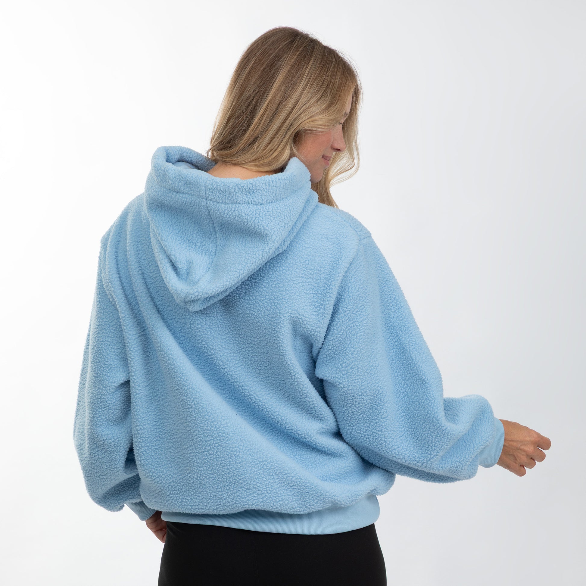A woman wearing a light blue sherpa fleece hoodie, shown from the back and side against a plain white studio background.