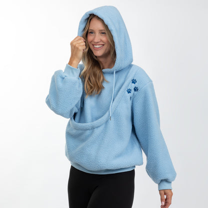 A woman wearing a light blue sherpa fleece hoodie with a drawstring hood and a small blue paw print graphic on the left chest, paired with black leggings, against a plain white studio background.