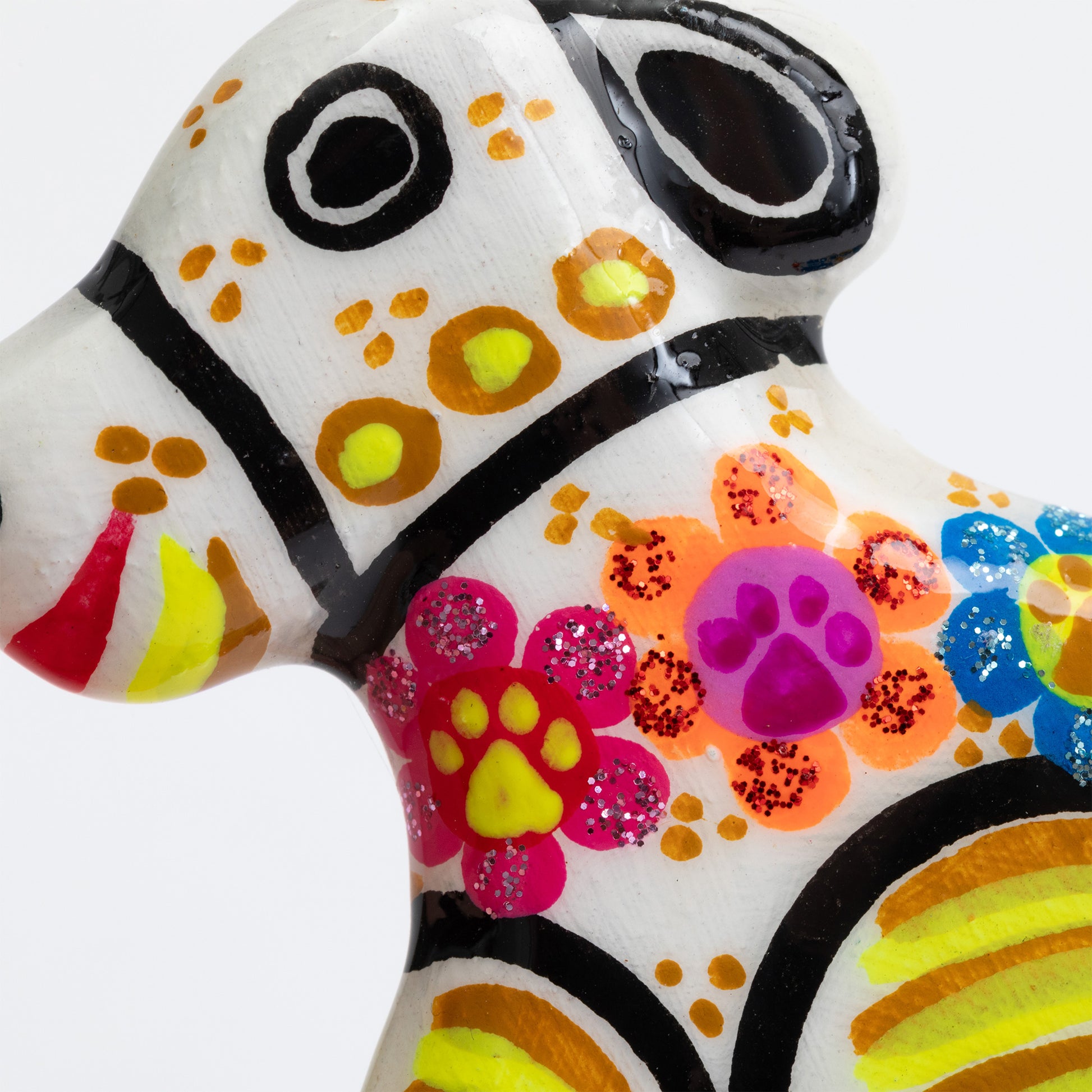 A close-up of a hand-painted ceramic dog figurine decorated with vibrant floral and paw-print patterns in pink, orange, yellow, blue, and purple on a glossy white base.