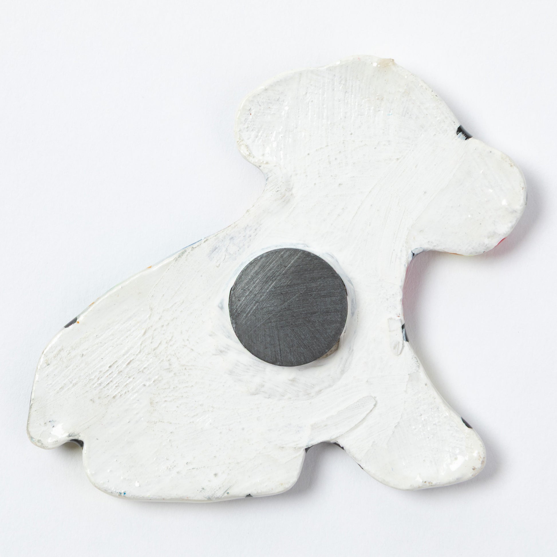 The back of a ceramic dog shaped magnet, against a white background.