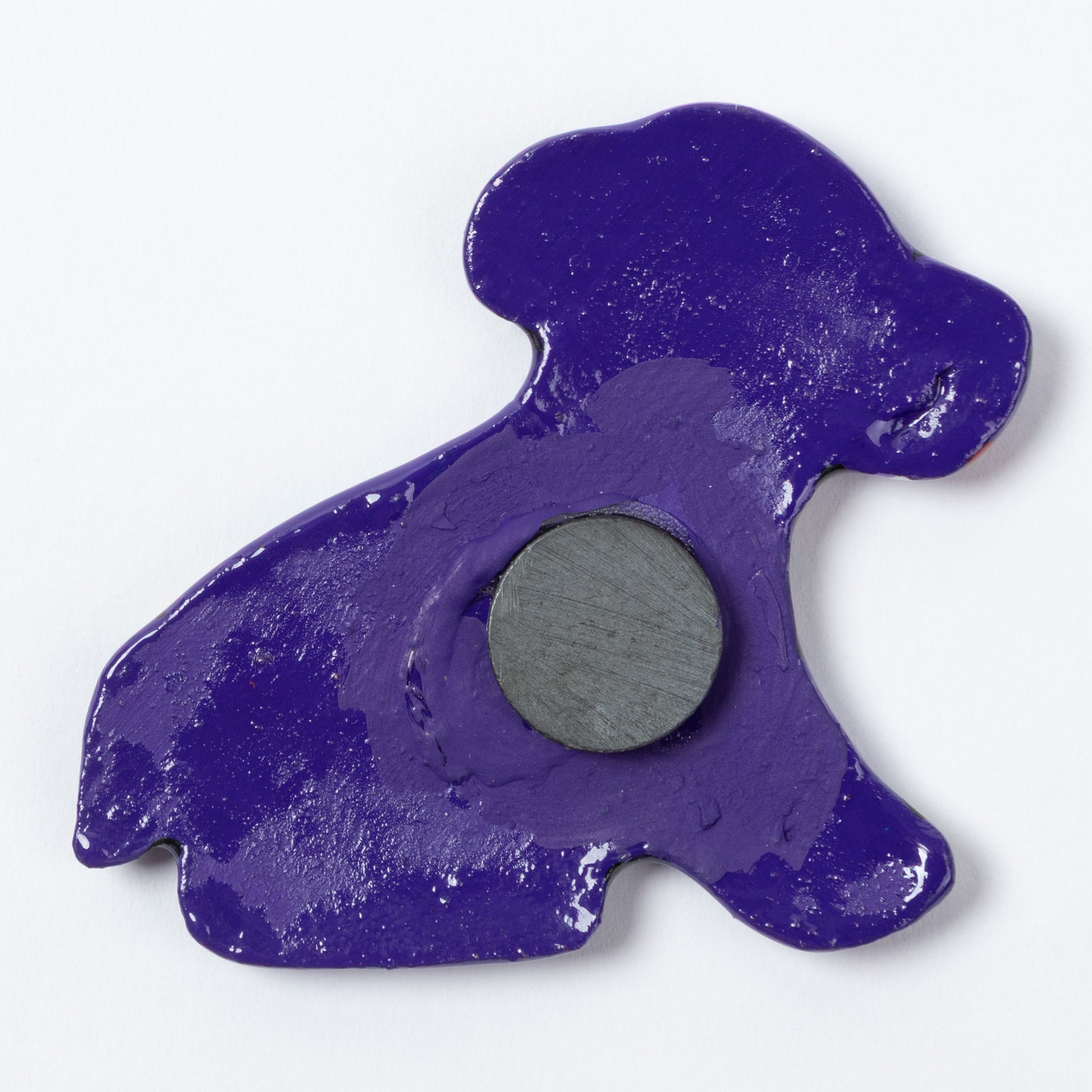 The purple back of a dog shaped ceramic magnet against a white background.