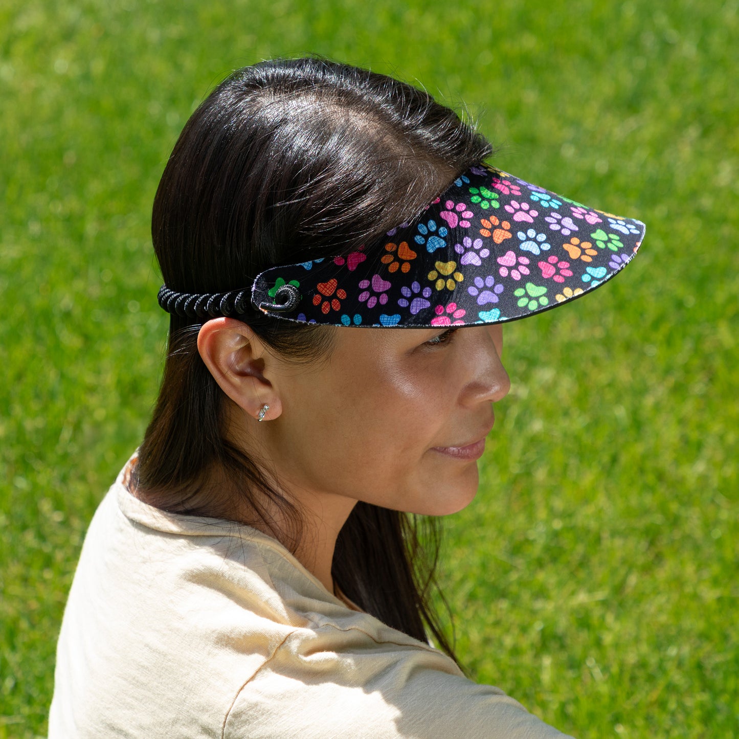Person wearing a colorful paw print visor against a green grass background