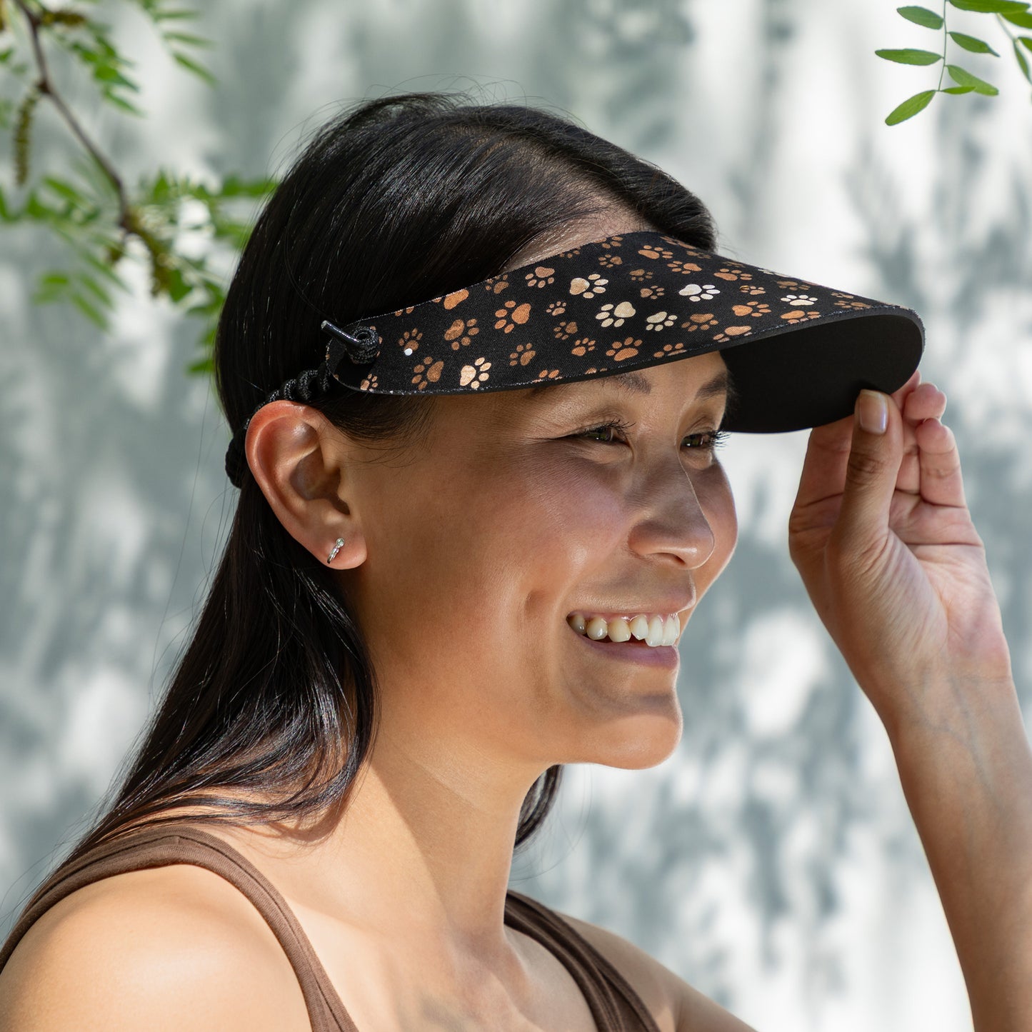 Woman wearing a black visor with brown paw prints against a blurred natural background