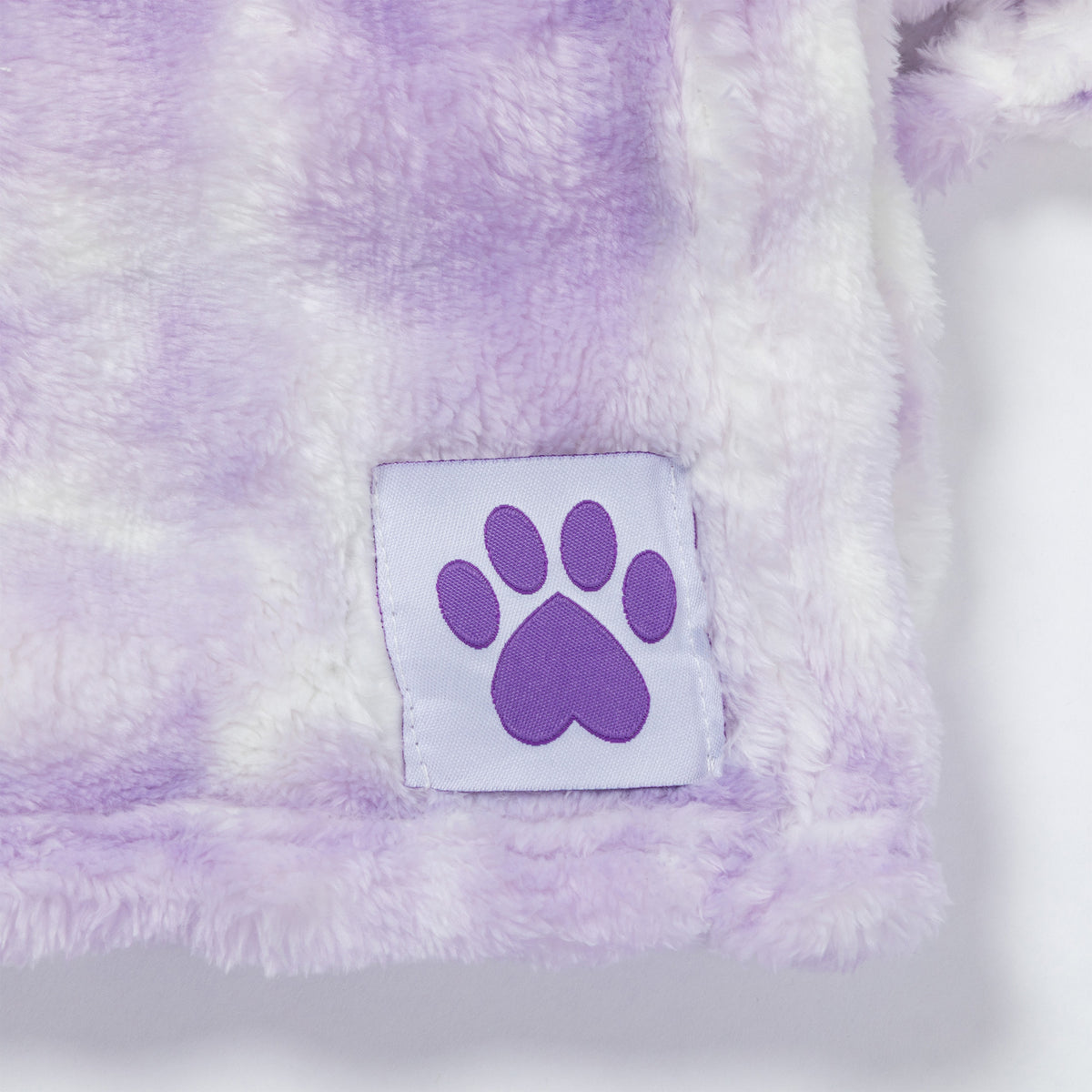 Close-up of a soft plush blanket with a lavender and white tie-dye pattern, featuring a square white patch with a purple paw print logo.