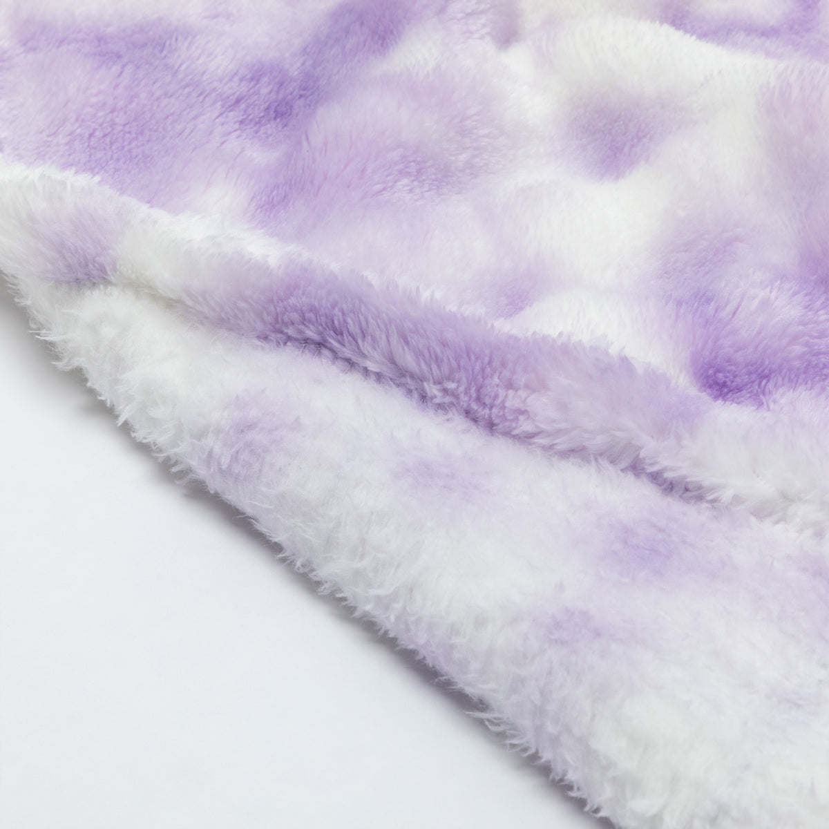 A close-up of a soft, fuzzy plush fabric in a lavender purple and white tie-dye pattern, folded over to show its texture.