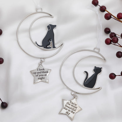 Two silver crescent moon and star ornaments displayed on a white fabric background. One ornament features a black dog silhouette on the crescent moon with a dangling silver star that reads 'I look up and think of you at night.
