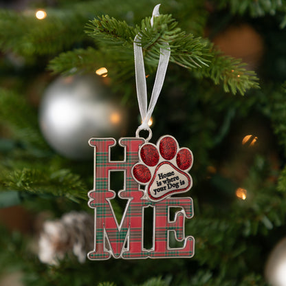 A Christmas ornament spelling 'HOME' in red plaid letters with a red paw print and the phrase 'Home is where your Dog is' on a tree branch with holiday lights.