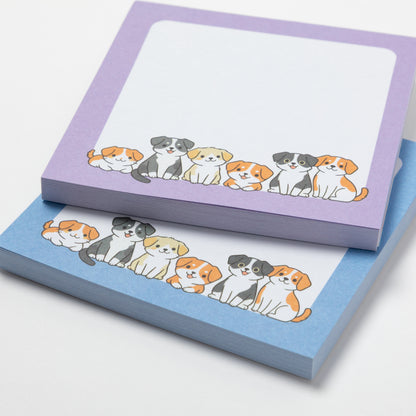 Two small notepad pads stacked on a white background. The top pad is lavender with a row of cartoon dogs along the bottom edge, and the bottom pad is light blue with the same dog illustration.