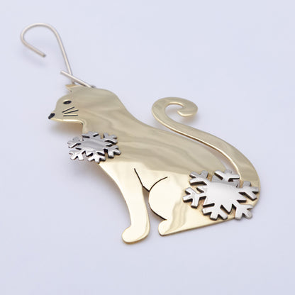 A polished gold-toned metal cat-shaped ornament with silver-toned snowflake accents on its chest and tail base, hanging against a plain light background.
