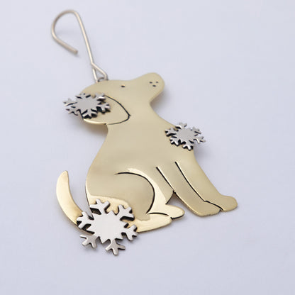 A polished gold-toned metal dog-shaped ornament with silver-toned snowflake accents on its chest and tail base, hanging against a plain light background.