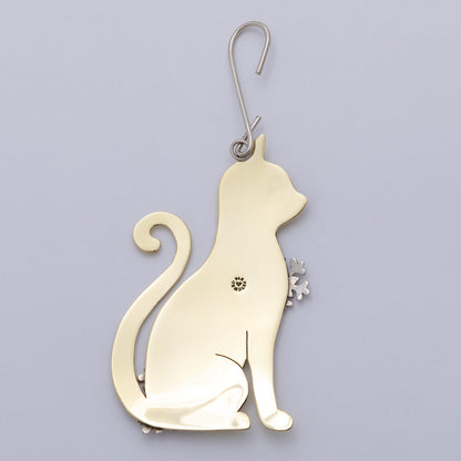 A polished gold-toned metal cat-shaped ornament with silver-toned snowflake accents on its chest and tail base, hanging against a plain light background.