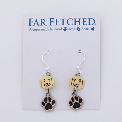 A pair of dangling earrings displayed on a white Far Fetched brand card. Each earring has a silver fishhook wire, a small gold-tone charm shaped like a dog face with black details and a pink tongue, and a larger dangling paw print charm with a black center and gold-tone border.