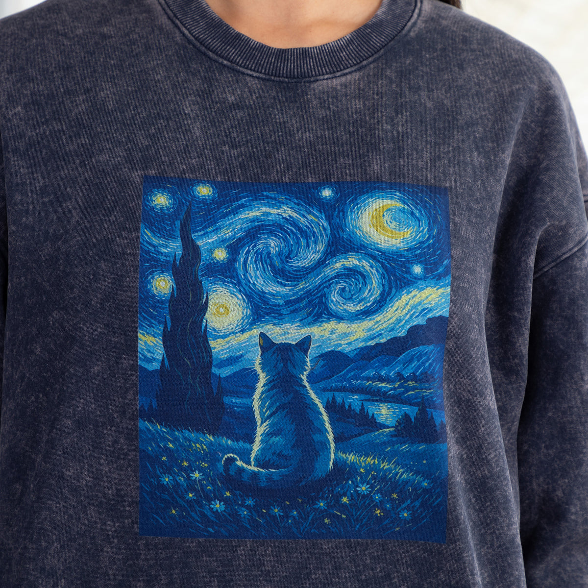 A close-up of a person wearing a dark gray crewneck sweatshirt featuring a square graphic print of a cat in a swirling blue and yellow Starry Night style landscape.