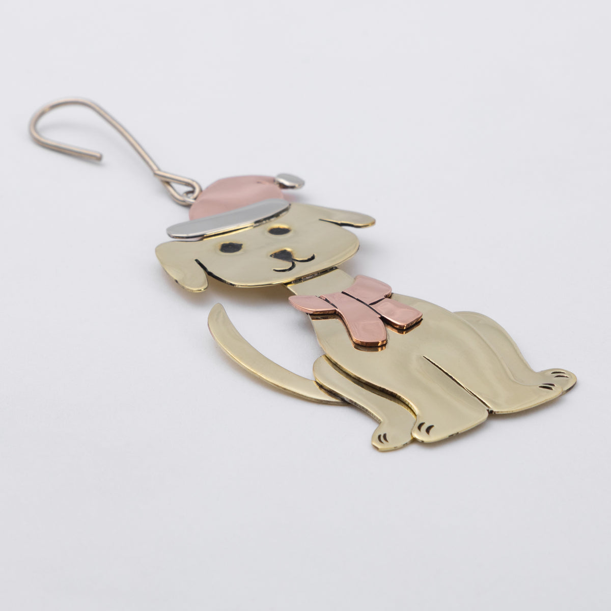 A brass dog-shaped ornament with a pink bow tie and hat, shown on a plain light gray background.