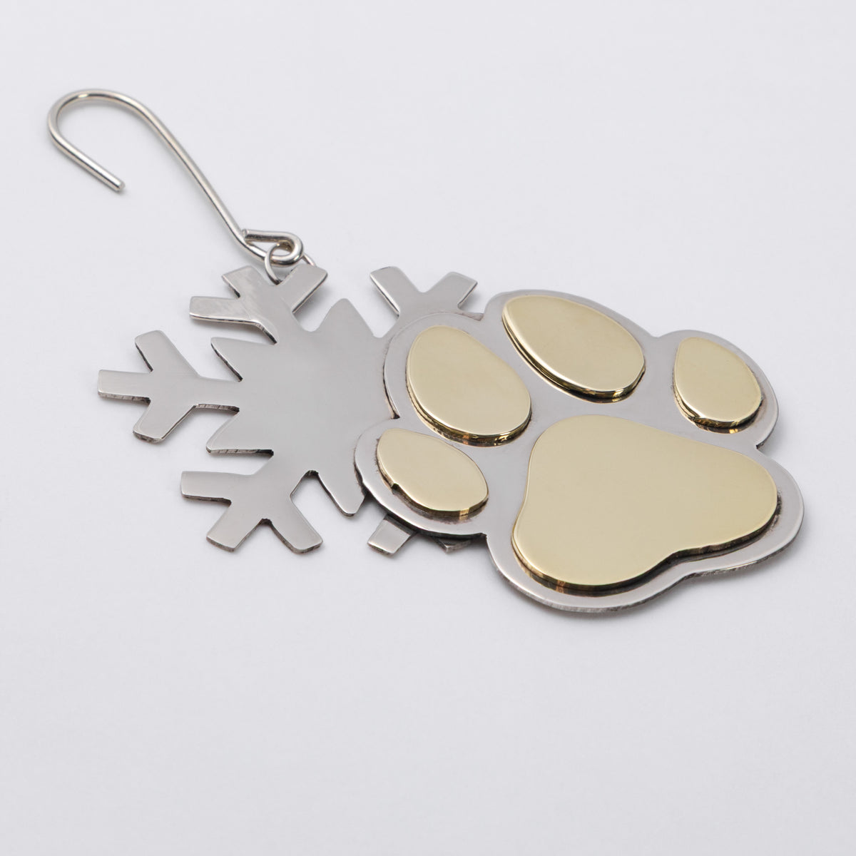A metal snowflake and paw print ornament with a gold-colored paw pad and gold-toned accents, attached to a silver-colored wire hook.