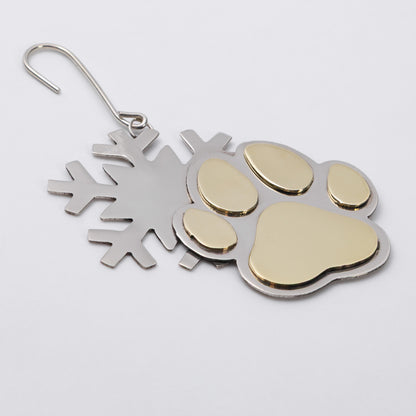 A metal snowflake and paw print ornament with a gold-colored paw pad and gold-toned accents, attached to a silver-colored wire hook.