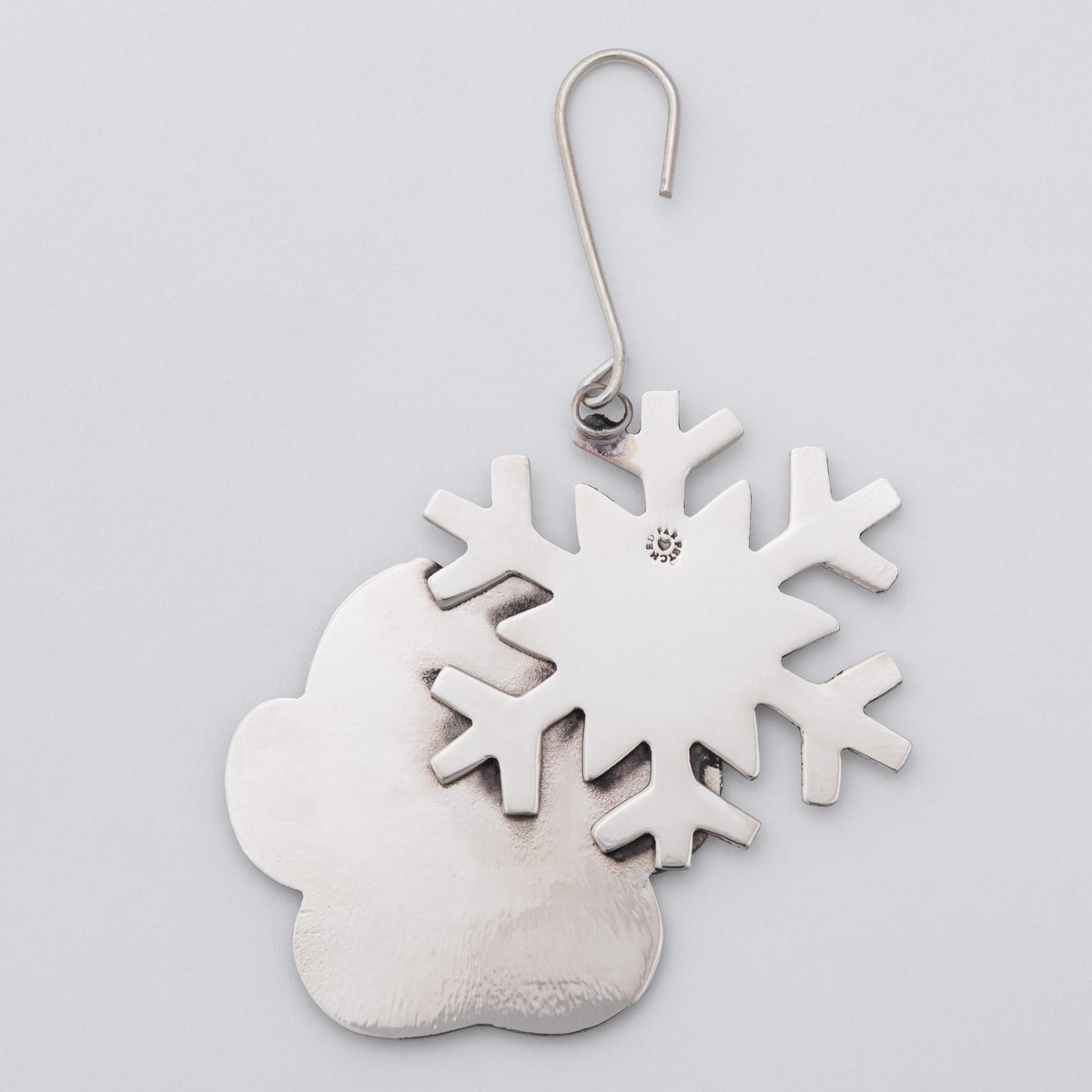 A metal snowflake and paw print ornament attached to a silver-colored wire hook.