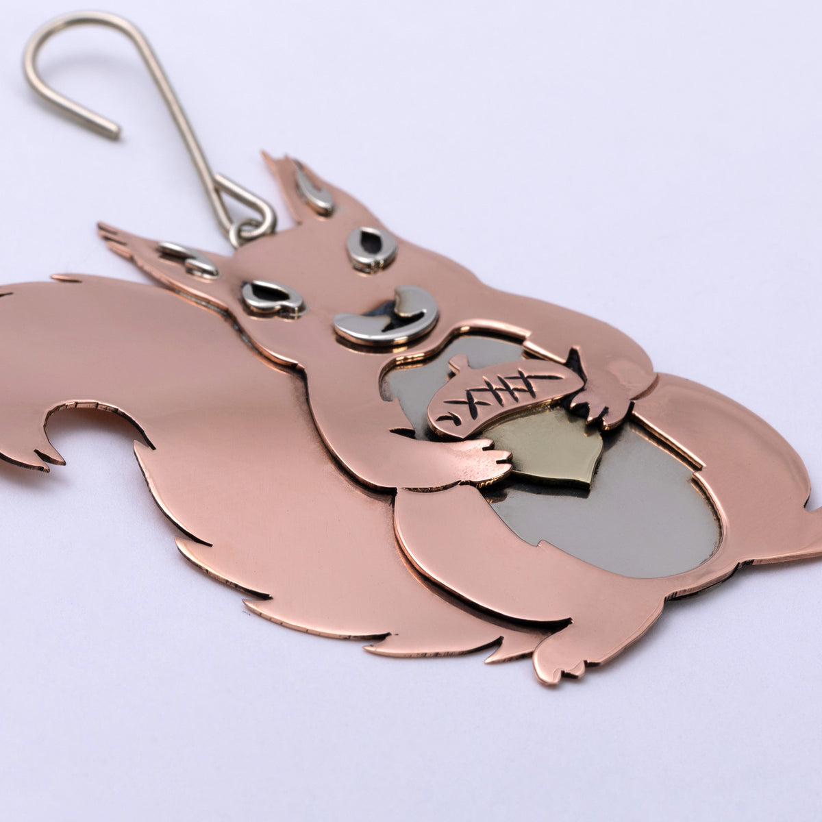 A copper-colored metal squirrel ornament holding an acorn, with a silver metal hanging hook at the top, shown on a plain light background.