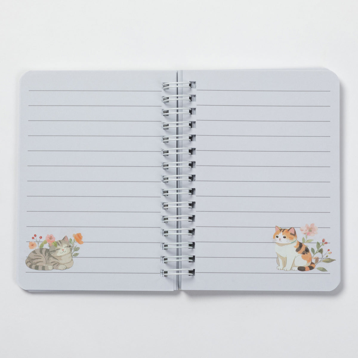 An open spiral-bound lined notebook with two watercolor cat illustrations decorated on the left and right pages, set against a clean white background.