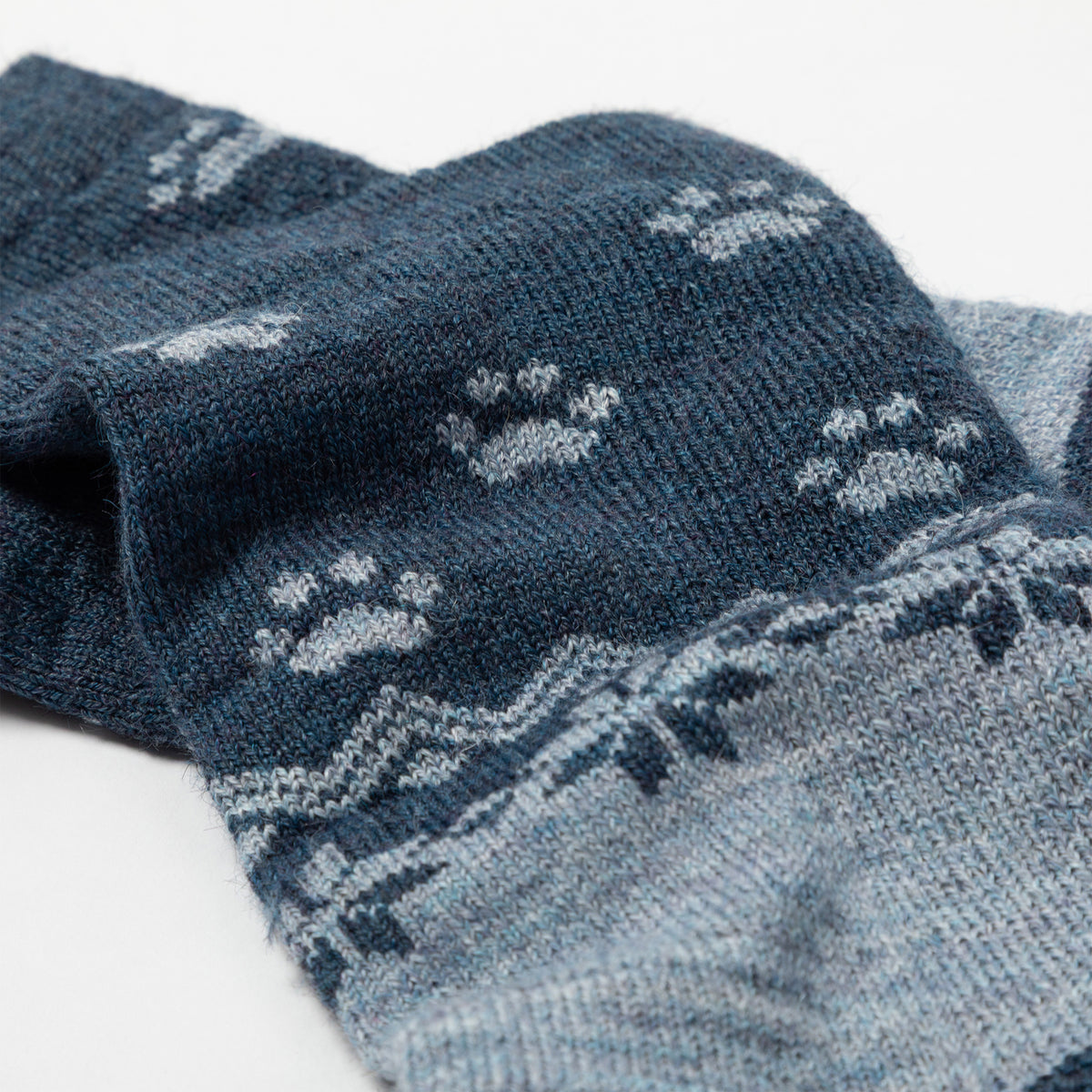 Close-up of a knit sock in dark navy blue with light gray paw print and geometric Fair Isle patterns, shown on a white background.
