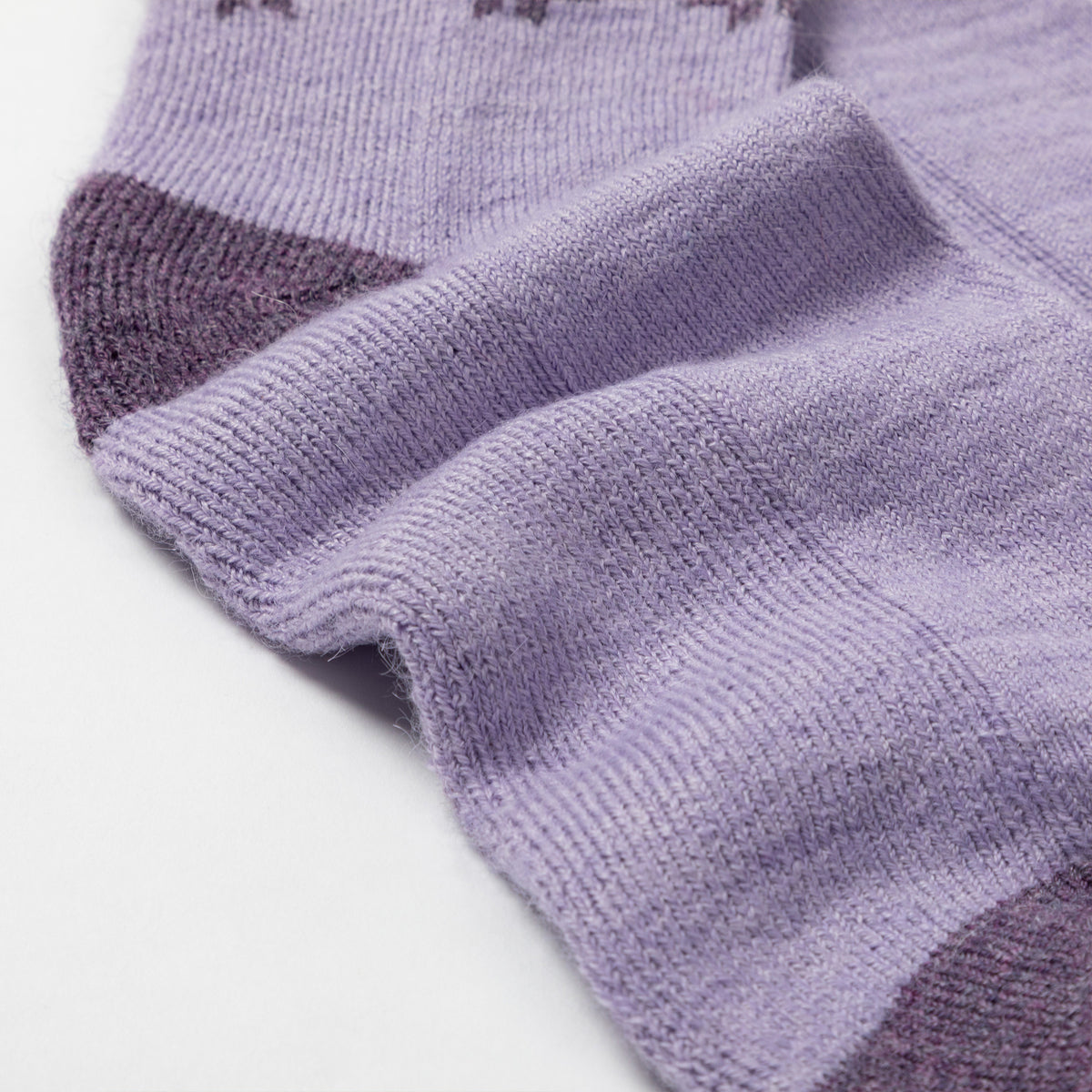 A close-up of a lavender knit sock with darker purple toe and heel sections, shown on a plain white background.
