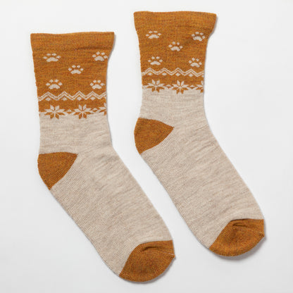 A pair of crew socks with a warm brown and cream knit pattern featuring paw prints and snowflake motifs, displayed on a clean white background.