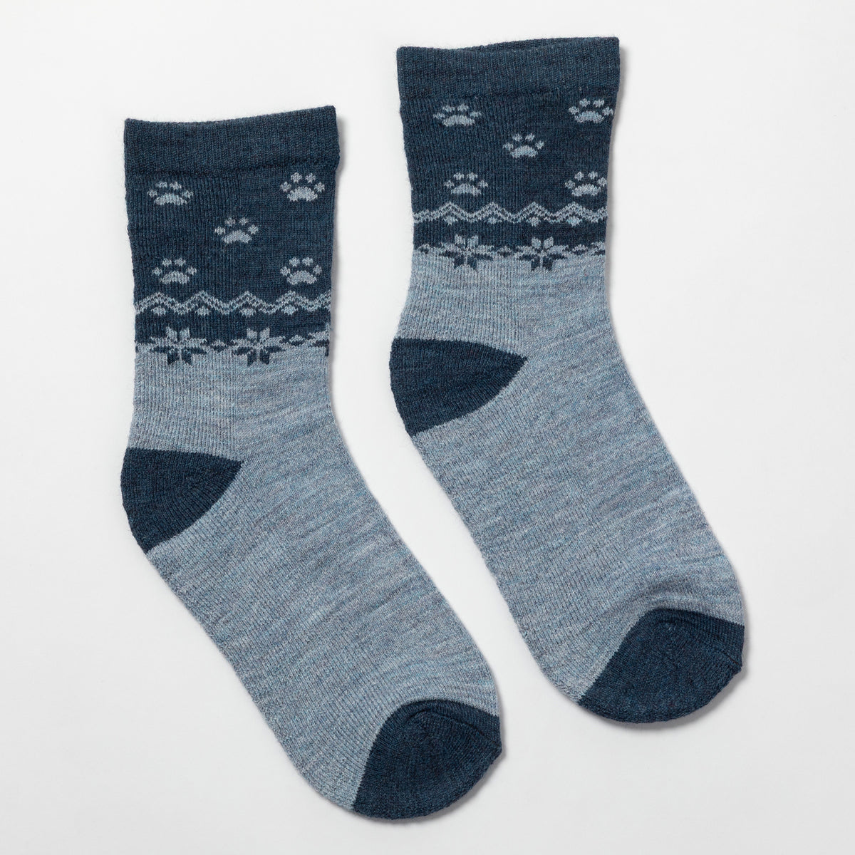 A pair of crew socks in heathered light blue with dark navy blue heels, toes, and cuffs, featuring a white knit pattern of paw prints and snowflakes on the upper leg.