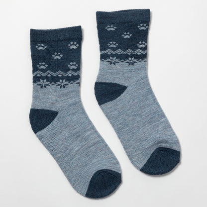 A pair of crew socks in heathered light blue with dark navy blue heels, toes, and cuffs, featuring a white knit pattern of paw prints and snowflakes on the upper leg.