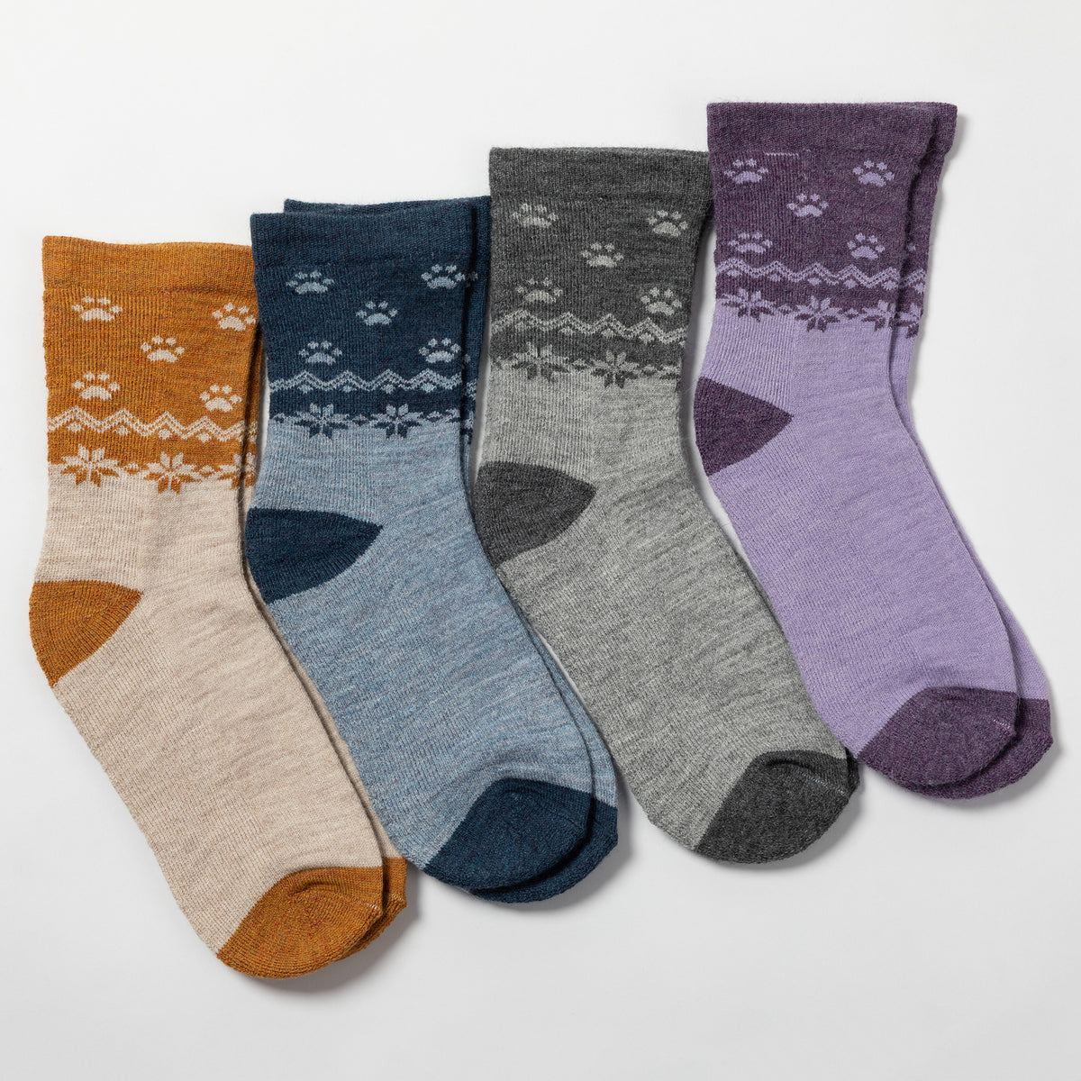 Four pairs of crew socks arranged in a fan shape on a light gray background. The socks come in mustard yellow, navy blue, heather gray, and lavender purple, each featuring a white Nordic/fair-isle pattern on the upper section and matching colored heels, toes, and cuffs.
