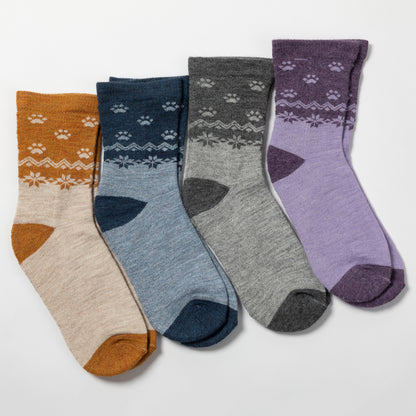 Four pairs of crew socks arranged in a fan shape on a light gray background. The socks come in mustard yellow, navy blue, heather gray, and lavender purple, each featuring a white Nordic/fair-isle pattern on the upper section and matching colored heels, toes, and cuffs.
