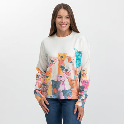 A woman wearing a cream-colored crewneck sweater featuring a colorful, all-over print of various dog faces on the front and sleeves, paired with blue jeans against a plain white studio background.