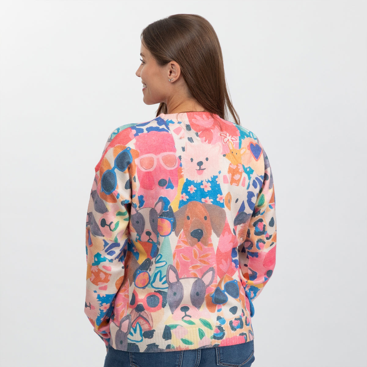 A woman shown from the back wearing a long-sleeve crewneck sweater with a colorful cartoon dog print, paired with blue jeans against a plain white background.