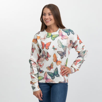 A woman modeling a cream-colored crewneck sweatshirt with a colorful butterfly print, paired with blue jeans, against a plain light gray background.