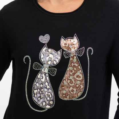 A close-up of a black long-sleeve top featuring a rhinestone-embellished graphic of two stylized cats facing each other, one in silver-gray and one in brown, with a small heart above them.